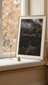 Framed artwork on a windowsill with a candle and small bell.