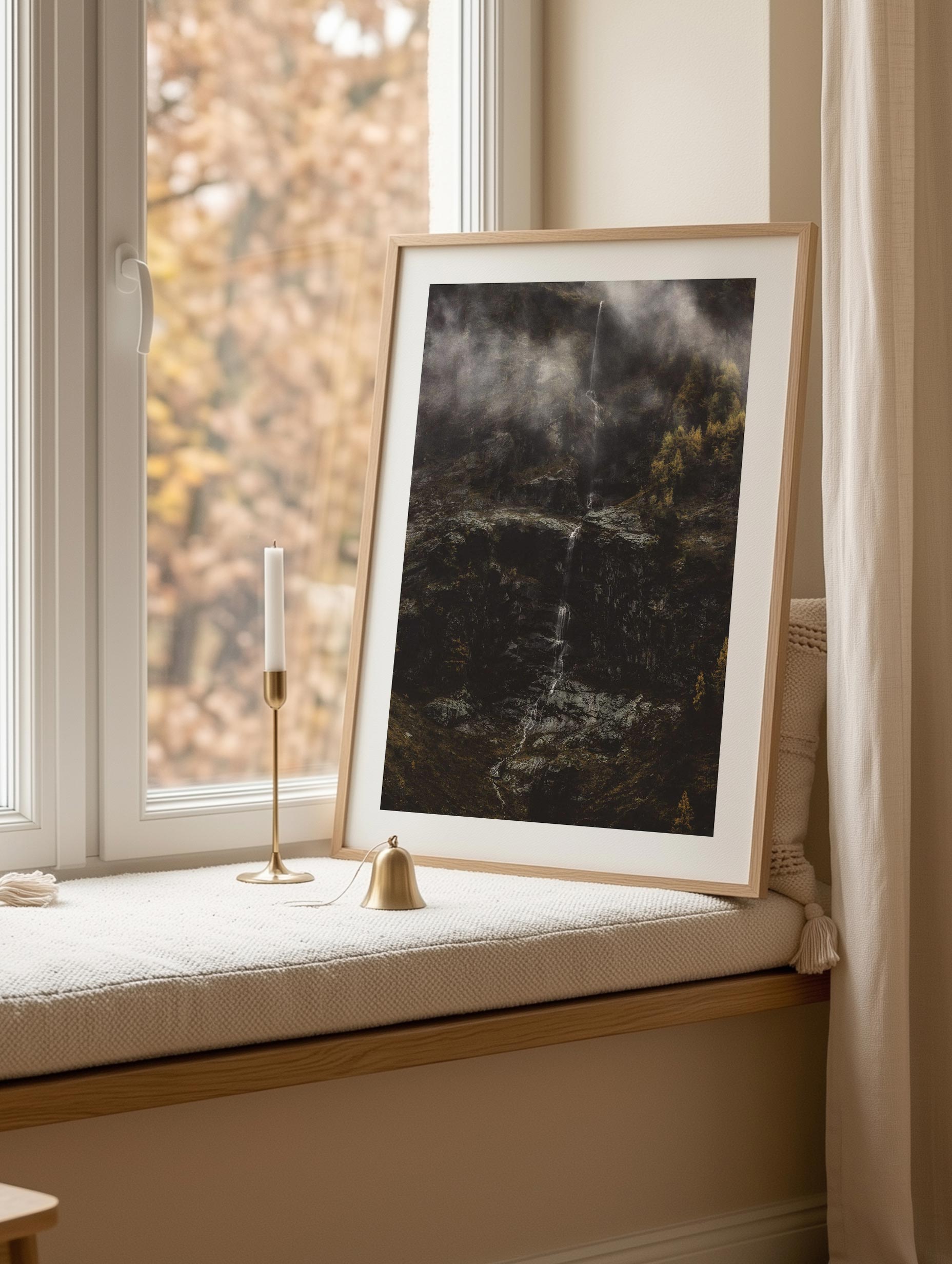 Framed artwork on a windowsill with a candle and small bell.